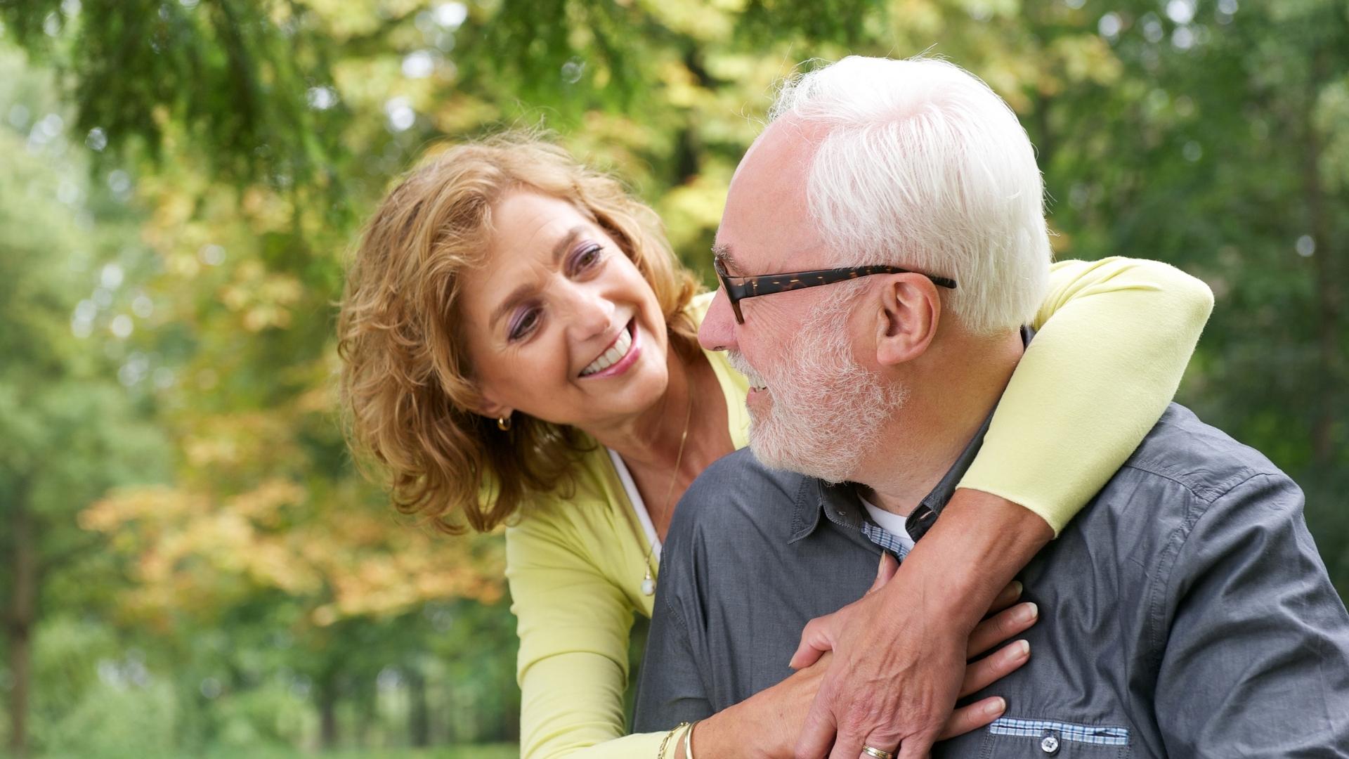 An older couple smiling and embracing outdoors.